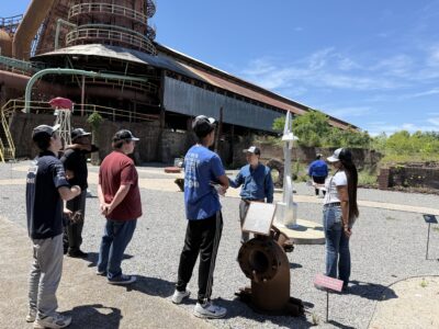 A group of student takes in the view of a retired historic foundry.