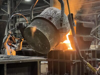 A worker in protective gear pours molten metal.
