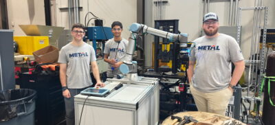 Students pose with a robotic arm in a university lab.