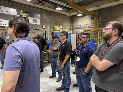 A tour group looks on as a tour guide speaks in a manufacturing lab