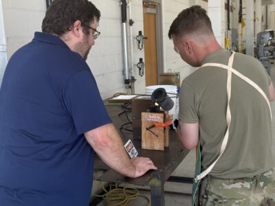 A service member pours molten tin into a sand mold.