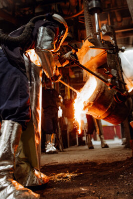 A metalworker pours molten metal from a crucible.